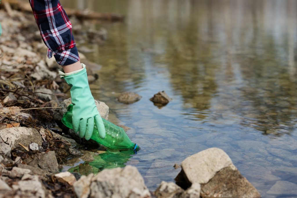 Image of individual collecting plastic waste from a river.